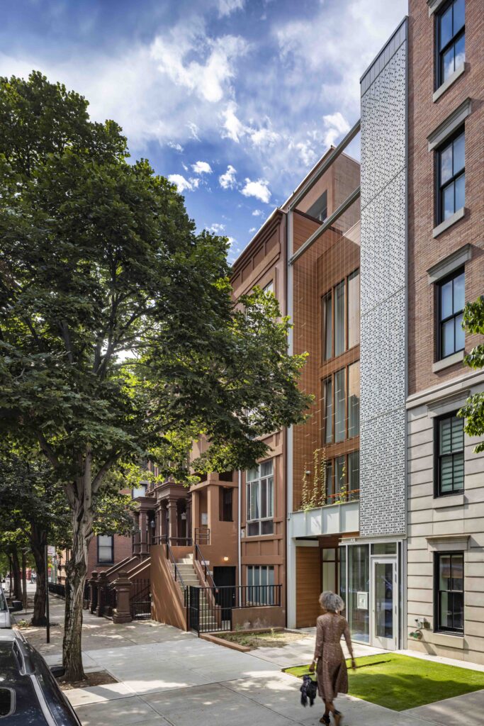 A photograph of a tree, sidewalk, and townhouse in Harlem.