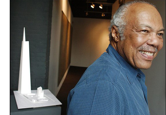 J. Max Bond, smiling and facing to the right, with an architectural model to the right.