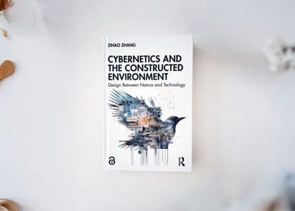 A book titled Cybernetics and the Constructed Environment: Design Between Nature and Technology by Zihao Zhang, lying flat on a light-colored surface. The cover features abstract artwork of a bird integrated with architectural and digital motifs.