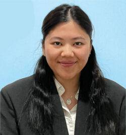 Headshot of Xiao Lin Wang, alumna of the Spitzer School of Architecture, smiling at the camera while seated in front of a sky blue background, dressed in a black blazer.