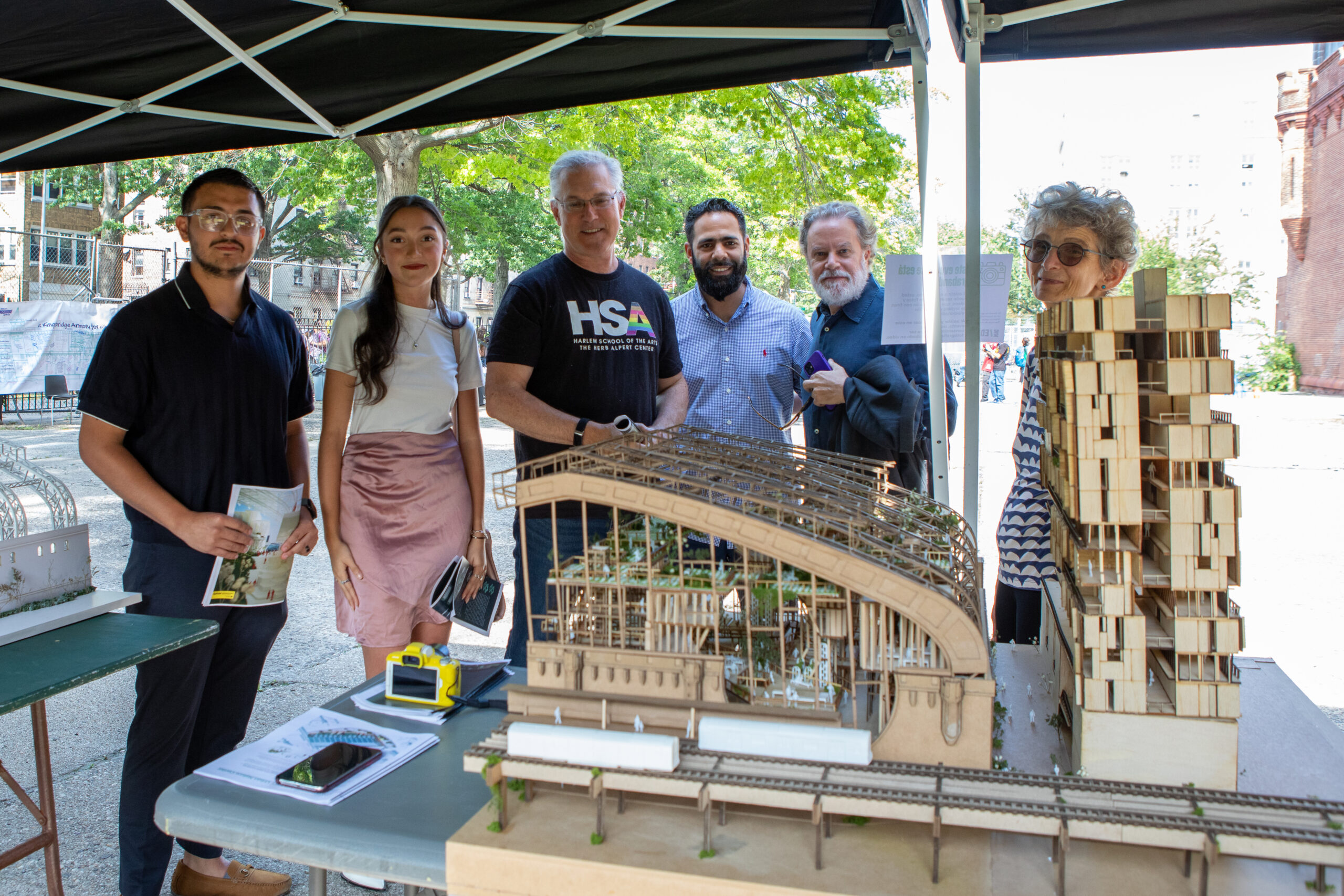 Five individuals, including two B. Arch students, all smile while standing behind an architectural model.