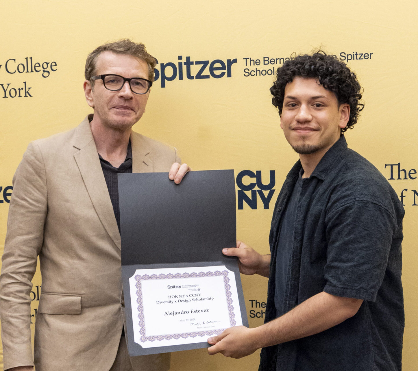 Faculty member and student standing and both holding an awards certificate in front of the Spitzer School step-and-repeat.