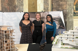 Three B. Arch students standing behind two architectural models.