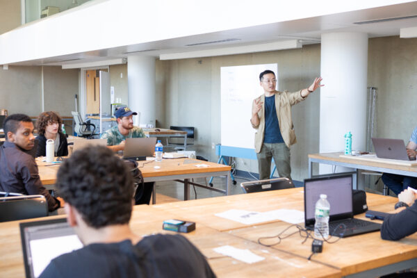 Photograph of Prof. Zhang standing in front of seated students during a lecture.