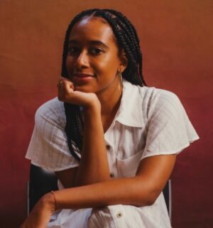 Headshot of Najha Zigbi-Johnson, looking to the left with her head resting on hand.