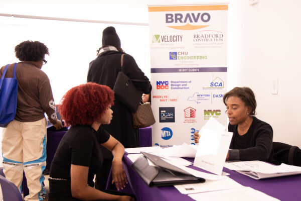 A student and a prospective employer seated at a table in discussion in front of a vinyl pop-up sign.