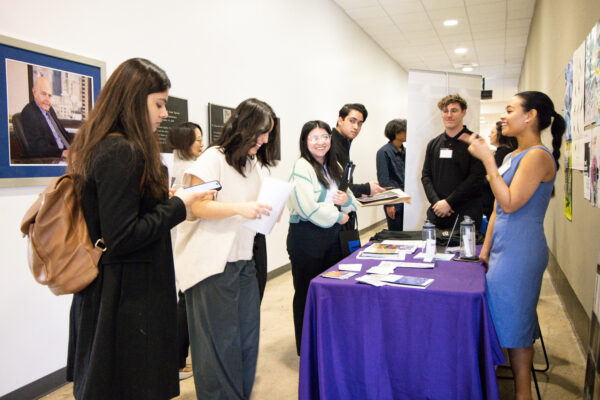 A prospective employer and students smiling standing at a booth at the Career Fair.