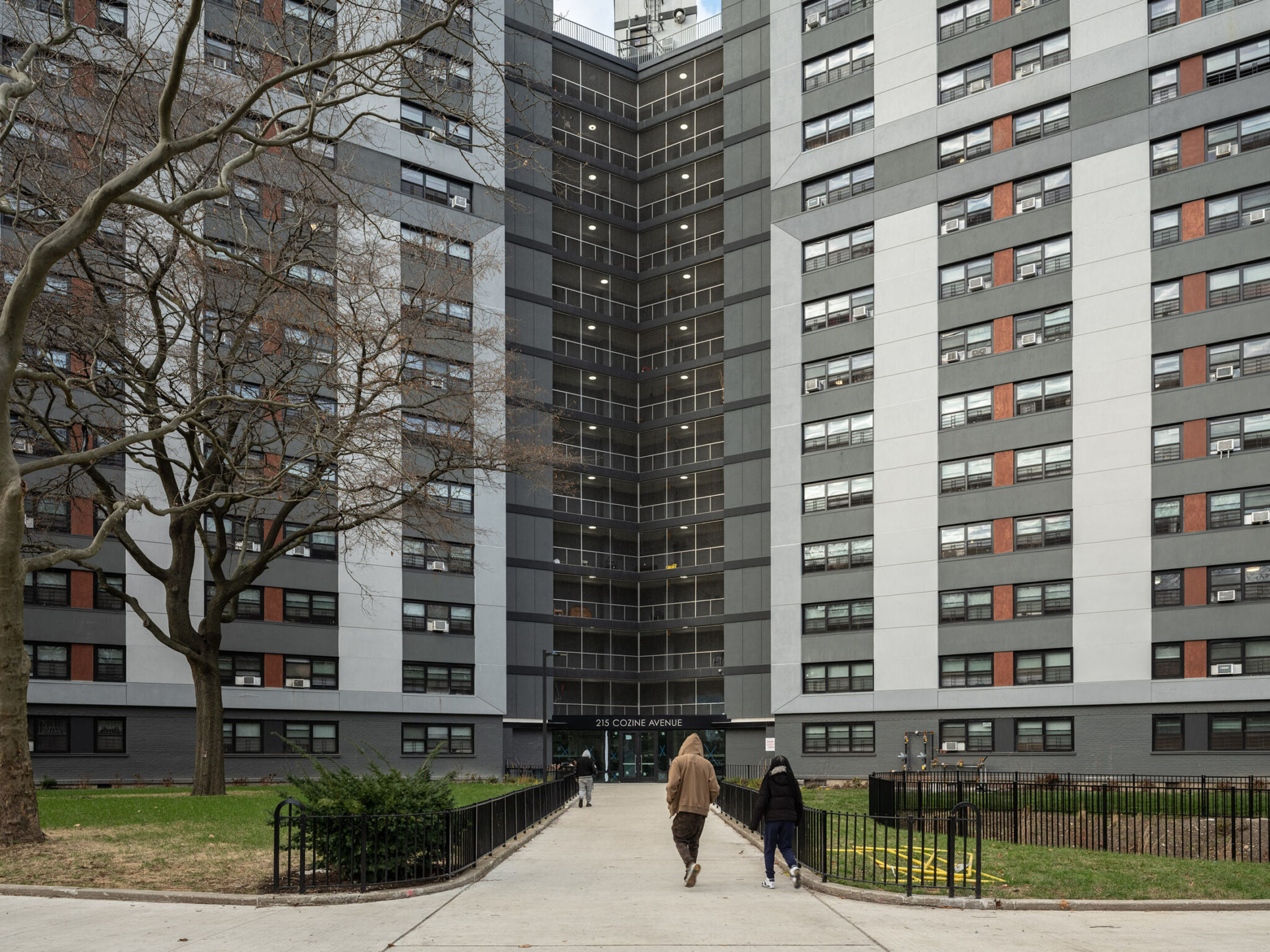 Photograph of NYCHA housing exterior with three people walking in front of the building.