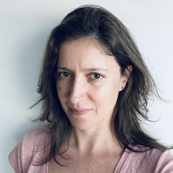 A woman with dark hair and brown eyes looks directly into the camera for a headshot photograph.