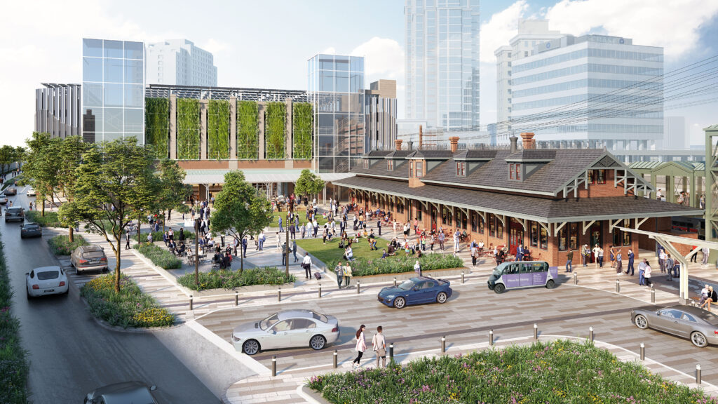 An architectural rendering of a public plaza in New Rochelle, New York, showing a blend of historic and modern design. In the foreground, a paved pedestrian area with stone tiling features small garden beds and low bollards separating the space from a slow-moving street with several cars. A historic red-brick building with a dark gabled roof serves as a central hub, surrounded by people sitting at outdoor tables or walking through a small green lawn. In the background, modern glass-and-steel structures, including one with a large vertical green wall (living wall) and solar panels on the roof, rise above the plaza. The scene is set under a bright, clear sky with taller city buildings and utility lines visible in the distance.