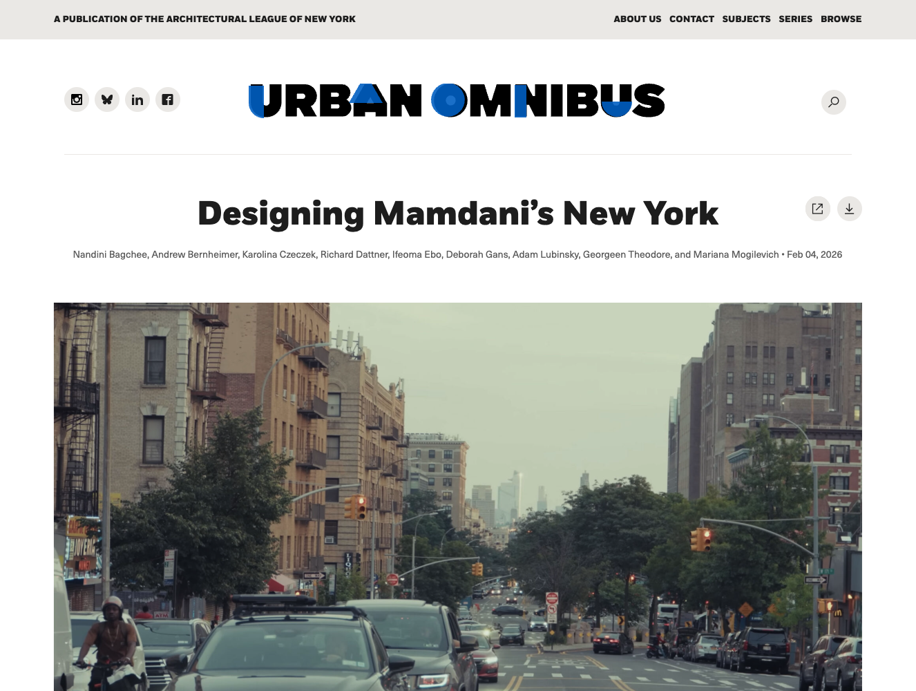 An eye-level, wide shot of a busy New York City street during the day, featuring heavy traffic and tall apartment buildings on both sides. In the foreground, several cars and a cyclist are visible, while the background shows more vehicles stretching into the distance under an overcast sky. The top of the image includes the digital masthead for 