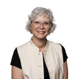 A professional headshot of a smiling woman with short, curly silver hair and clear-rimmed glasses, wearing a black shirt under a cream-colored button-down vest against a white background.