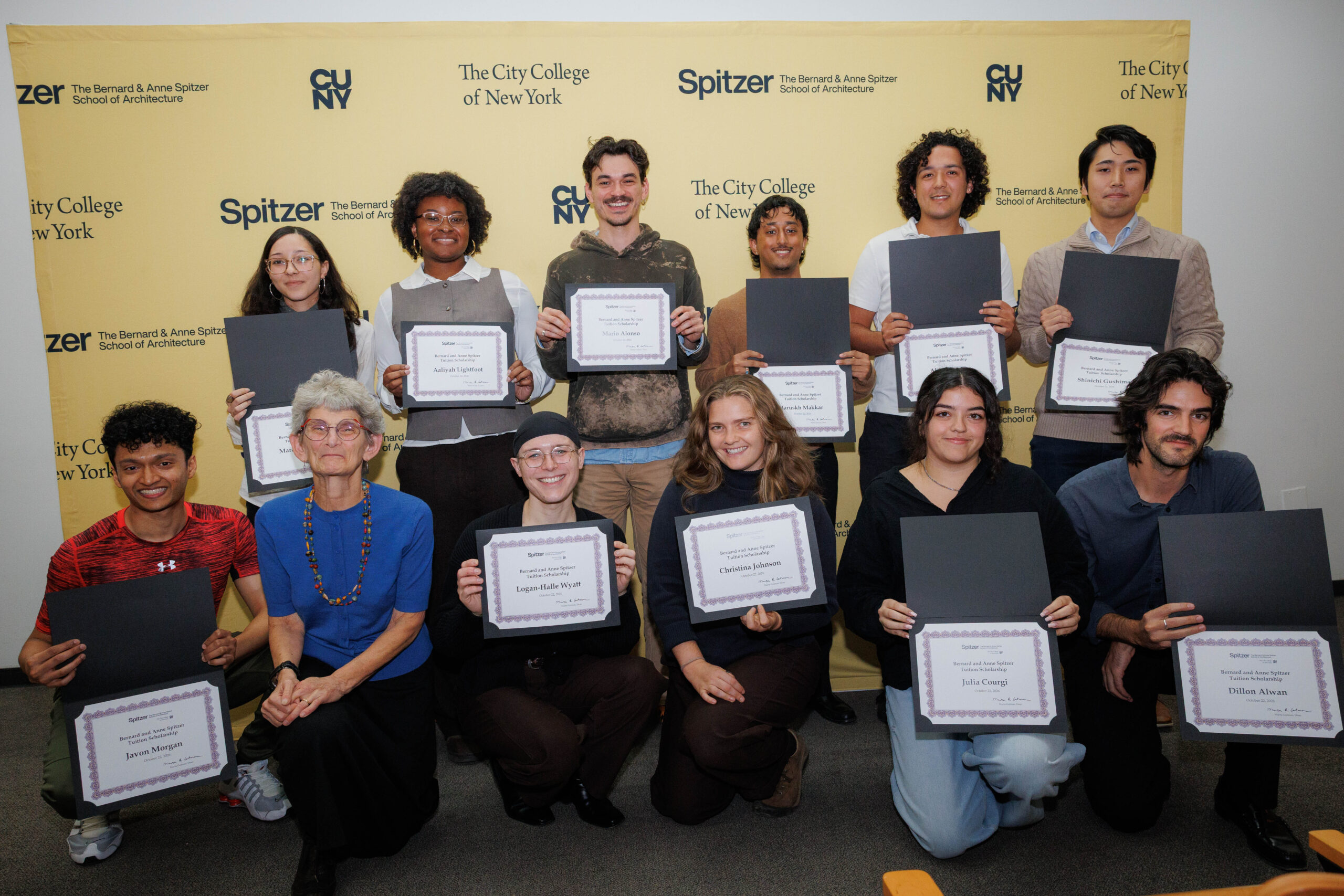 A group of students and faculty pose together holding their award certificates in front of a branded step-and-repeat backdrop for The City College of New York and the Bernard and Anne Spitzer School of Architecture.